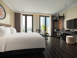 A hotel room with a large bed, a desk, a chair, a TV, and a balcony with a view of the city. - T Boutique Hotel (Hanoi)