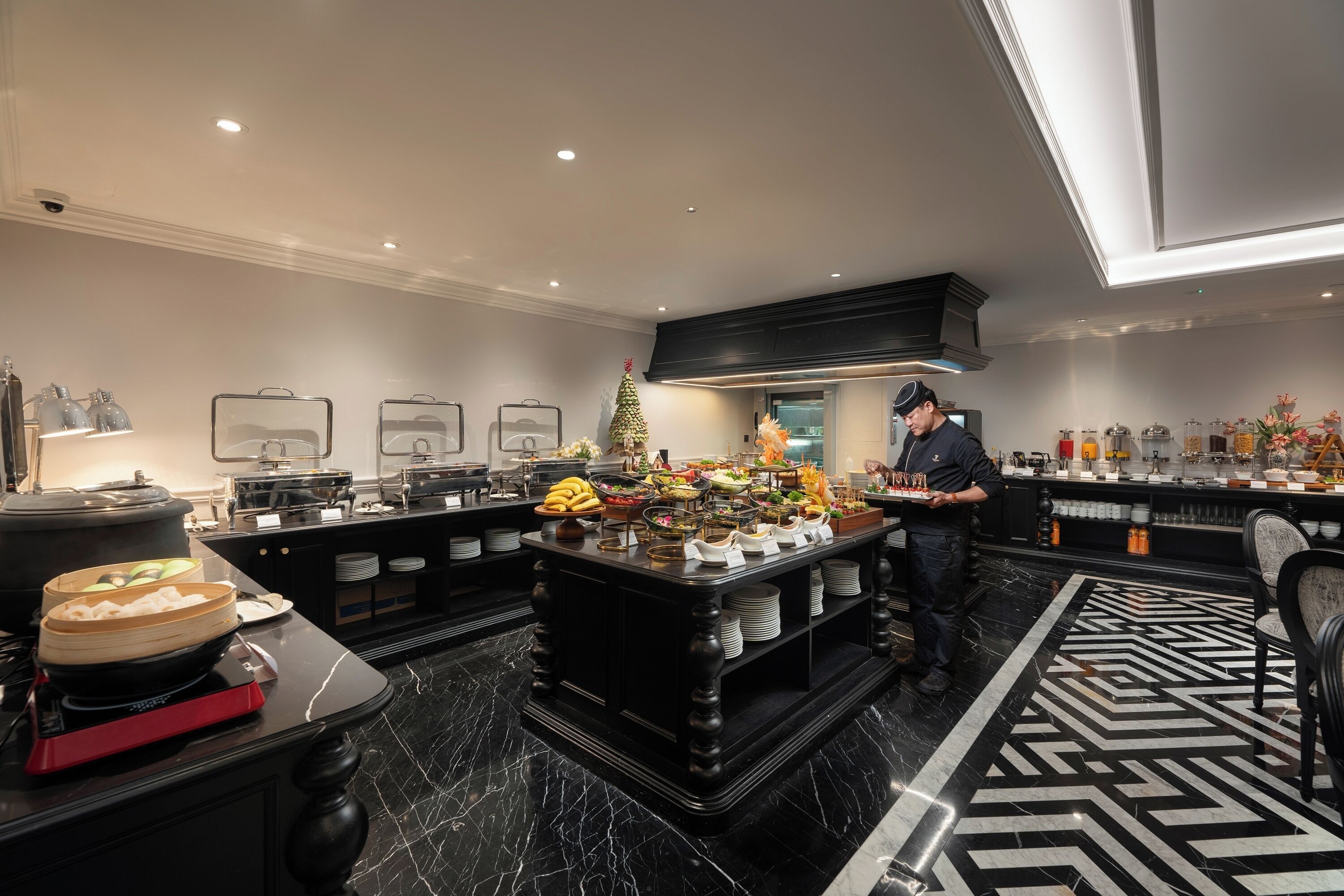 A hotel kitchen with a buffet setup, marble flooring, and a modern design.
