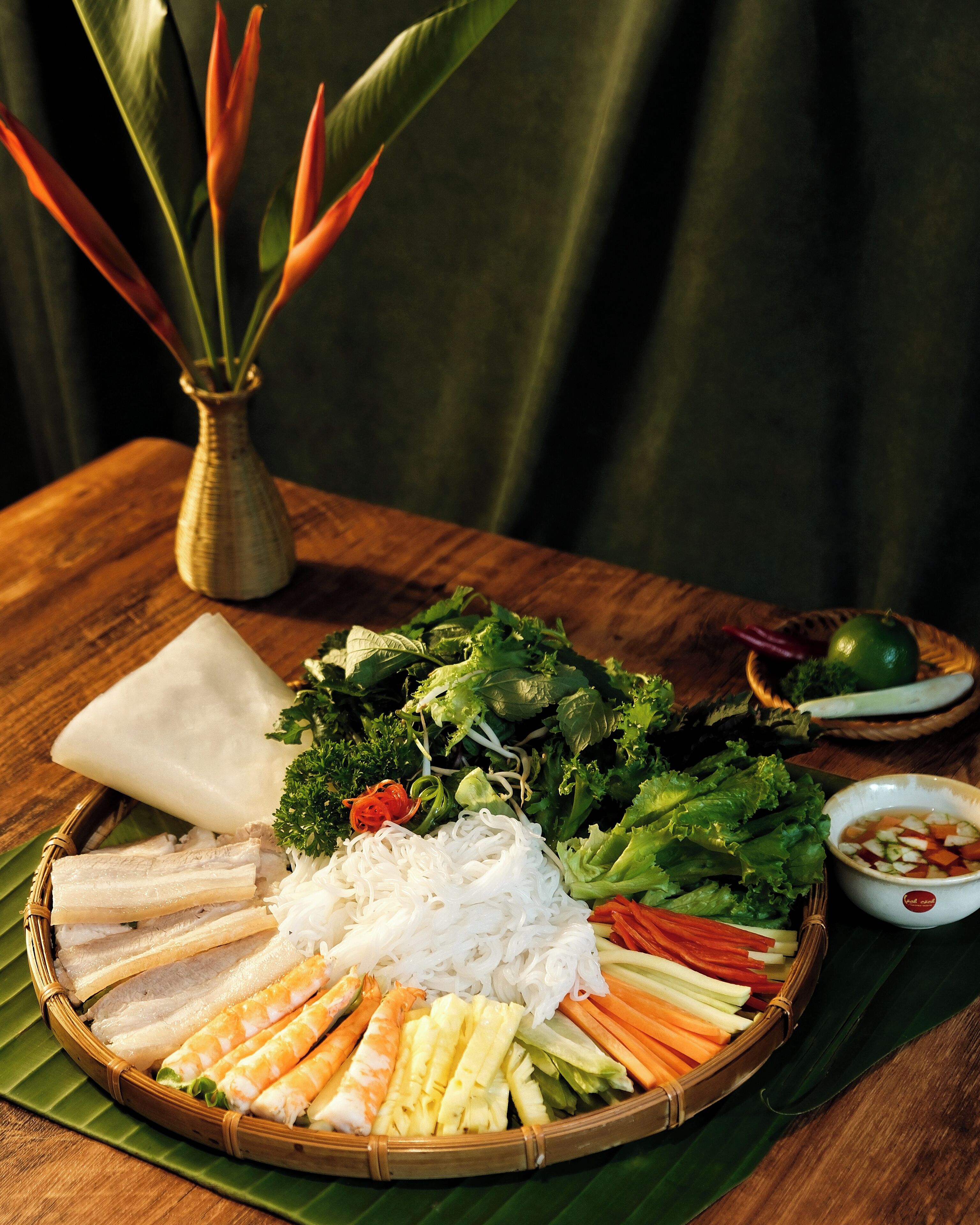 Une table garnie d’une variété de plats, notamment des légumes, des nouilles et de la viande, disposés sur une feuille de bananier.