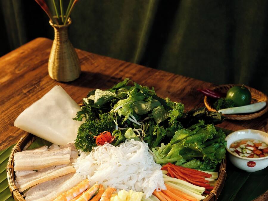 Une table garnie d’une variété de plats, notamment des légumes, des nouilles et de la viande, disposés sur une feuille de bananier.