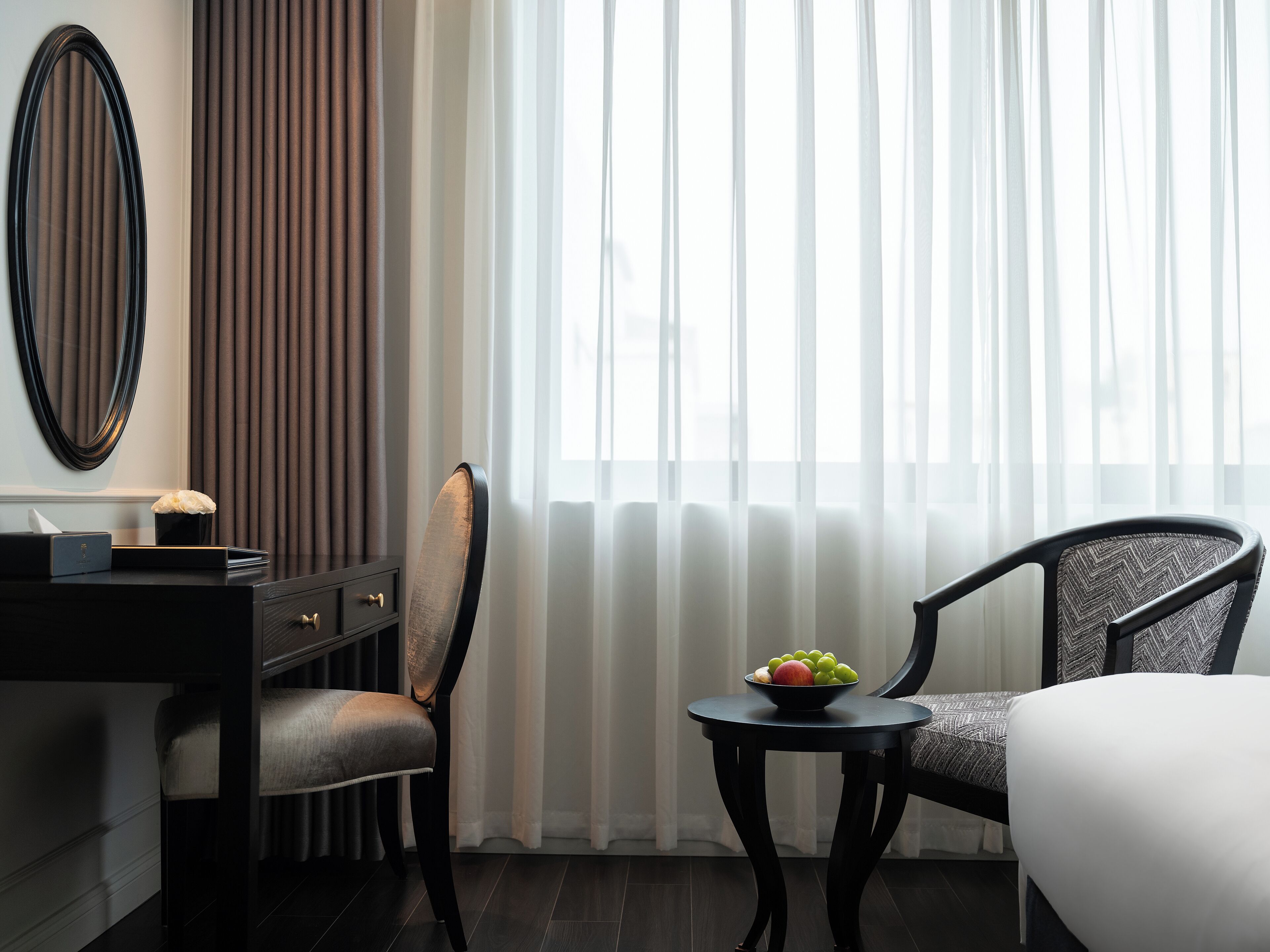 Une chambre d’hôtel avec un lit, deux chaises, une petite table avec des fruits, un miroir et une commode.