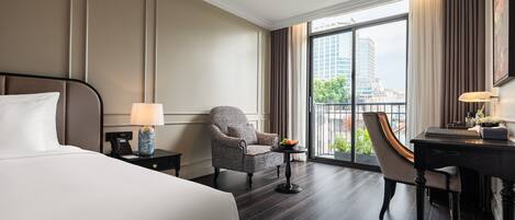 A hotel room with a large bed, a chair, a desk, and a view of the city through a large window.