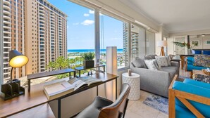 Ein modernes Wohnzimmer mit großem Fenster, das auf eine Skyline und einen Strand blickt.