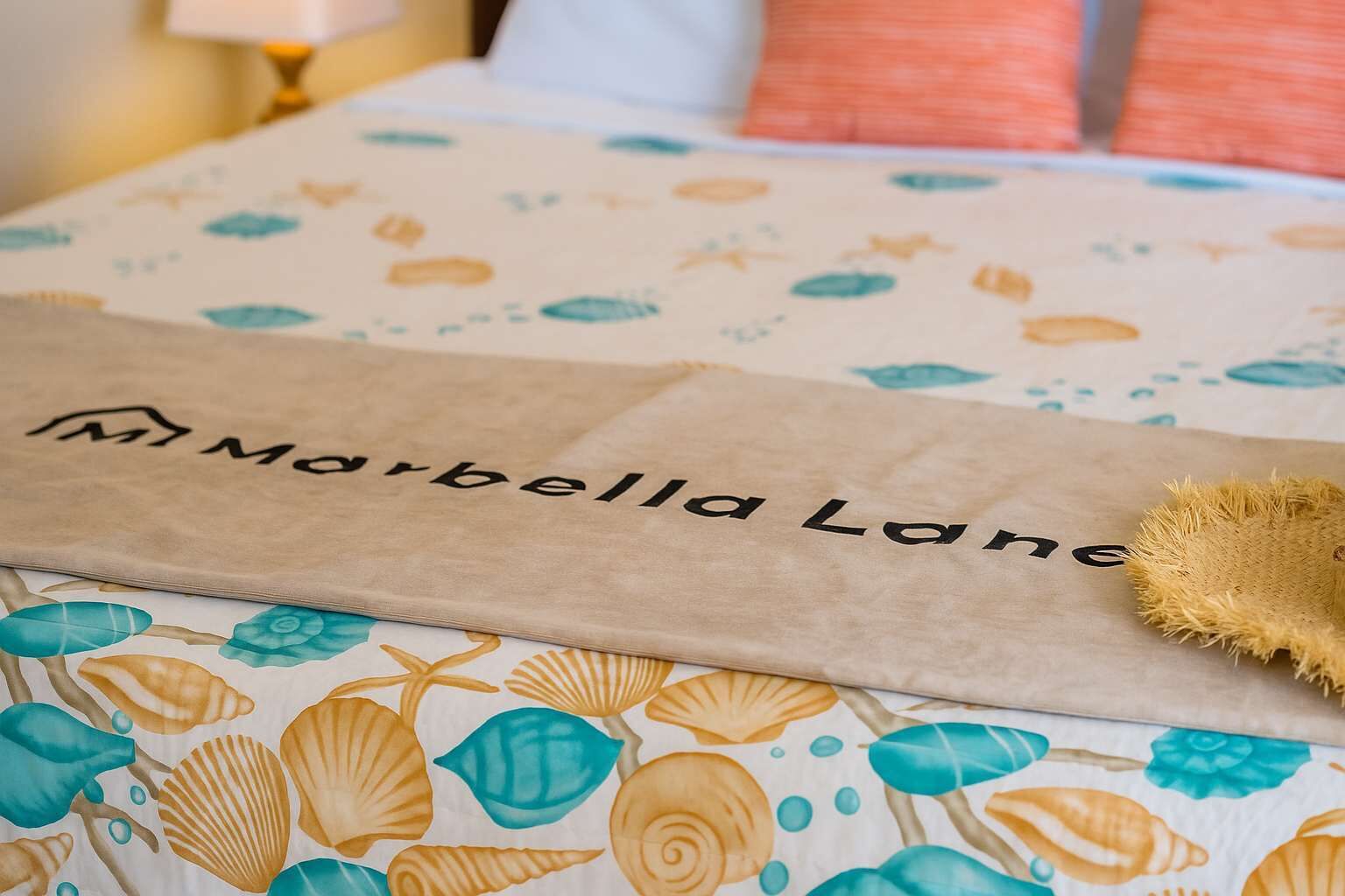 Un letto con una coperta a motivi e una busta di carta marrone con la scritta 'Marbella Lane'.