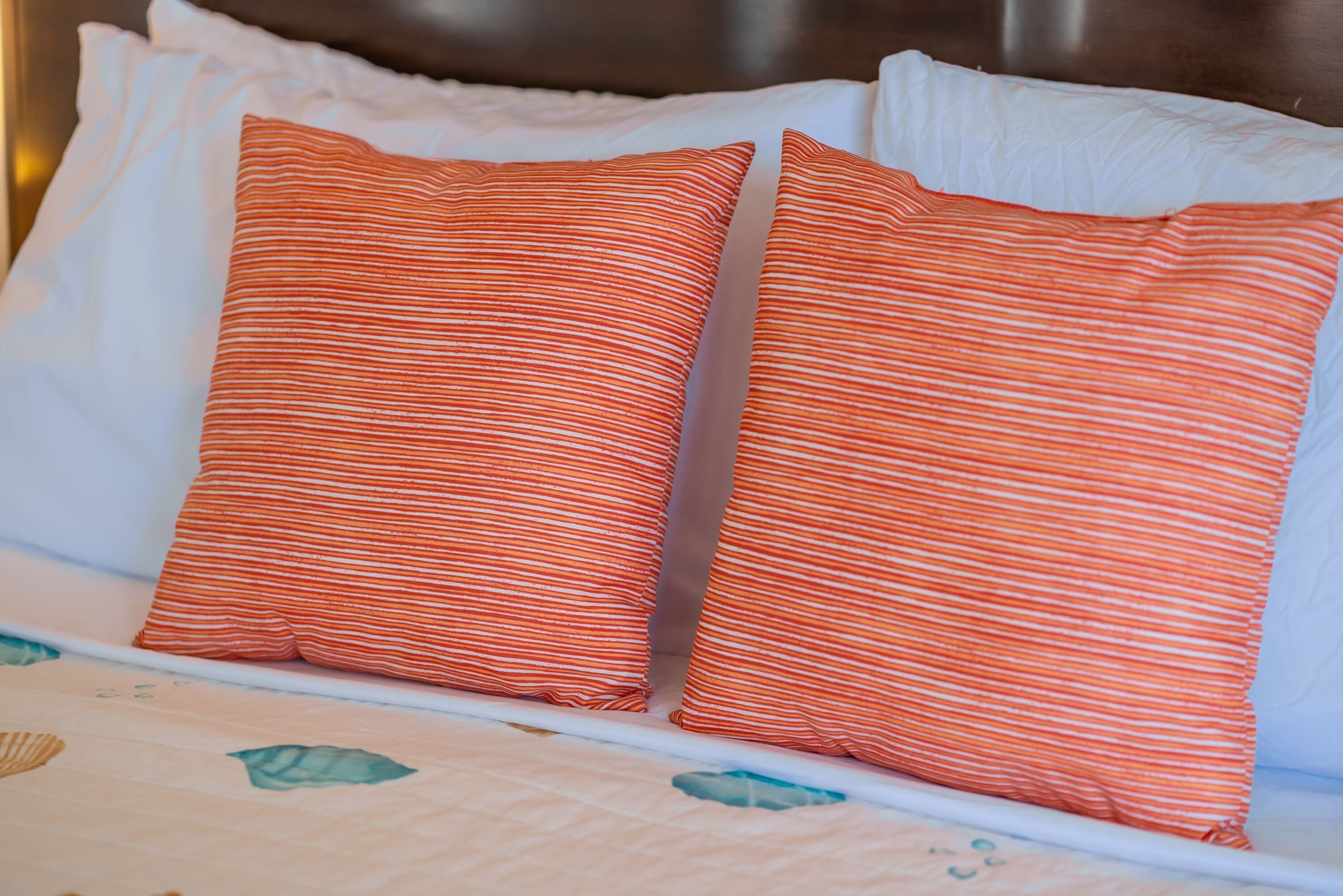 A bed with white pillows and two orange-striped pillows.