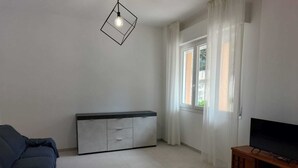 Olohuone, jossa on sohva, puinen TV-taso, kaappi ja ikkuna, jossa on verhot.