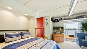 Une chambre à coucher avec un lit, une armoire en bois, une porte rouge et une vue sur un lac, visible à travers une porte vitrée.