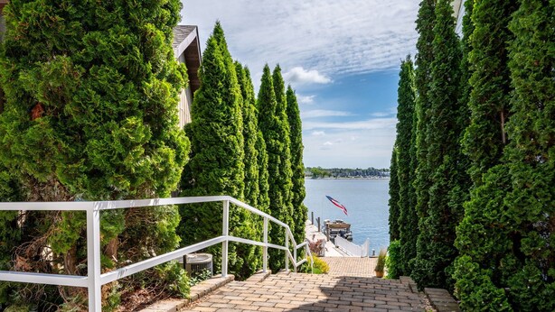 Un escalier menant à une jetée où flotte un drapeau, le tout entouré de grands arbres à feuilles persistantes.