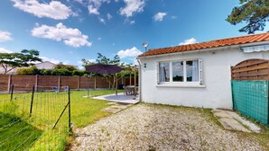 A white house with a tiled roof, a fenced backyard, and a gravel path leading to a patio area with outdoor furniture. - Nid Douillet Terre et Mer (Saint-Hilaire-de-Riez)
