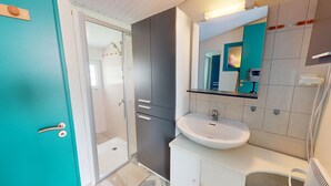 A modern bathroom with a glass shower enclosure, a white sink, and a mirror with a teal frame. - Nid Douillet Terre et Mer (Saint-Hilaire-de-Riez)