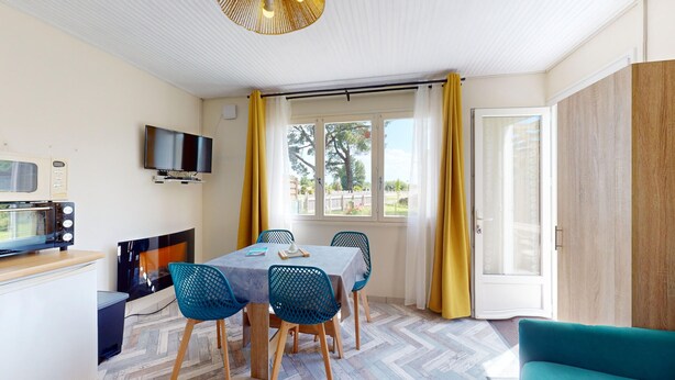 A compact room with a dining table, chairs, a TV, a microwave, and a sliding glass door leading to an outdoor area. - Nid Douillet Terre et Mer (Saint-Hilaire-de-Riez)