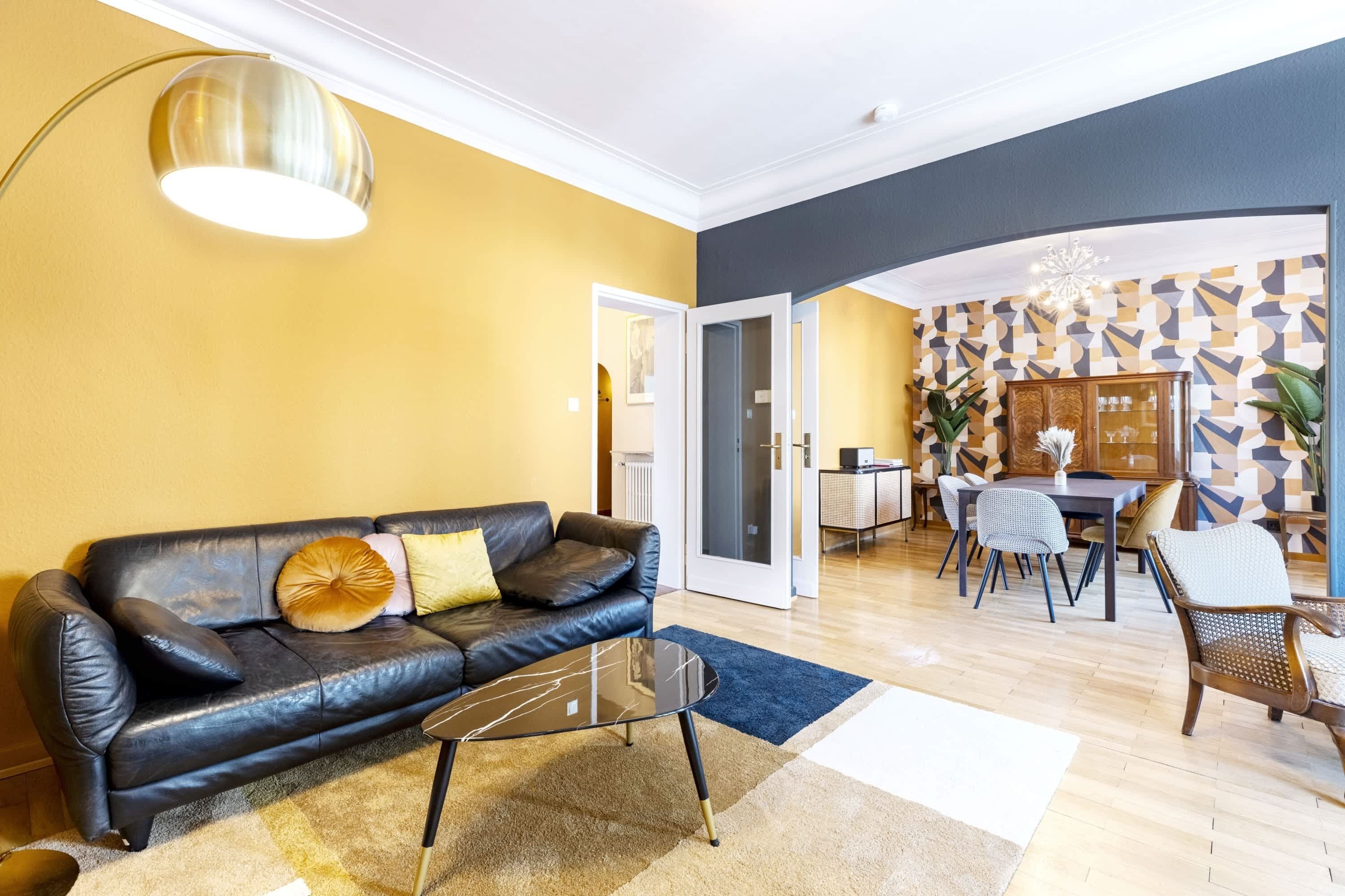 A living room with a black leather sofa, a glass coffee table, and a dining area with a table and chairs.