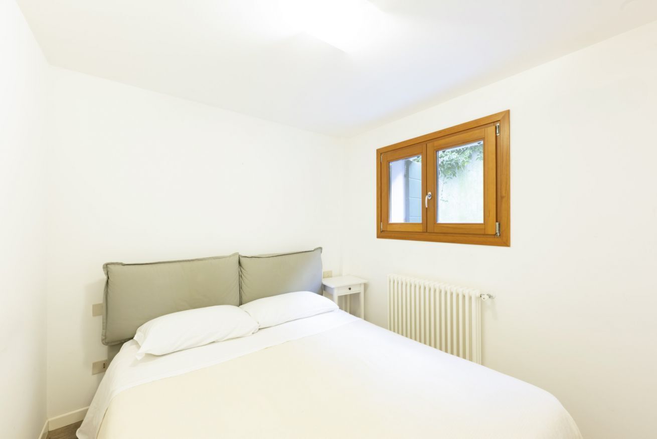 Une chambre à coucher avec un lit, une table de chevet, une fenêtre et un radiateur.