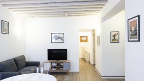 Een moderne woonkamer met een flatscreen televisie, een grijze bank, een marmeren tafeltje en lijstwerken aan de wanden.