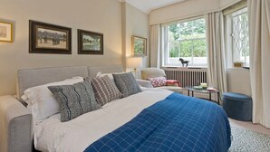 A hotel room with a large bed, a window with curtains, a radiator, and framed pictures on the wall. - Spacious Studio Flat, Holland Park (Greater London)