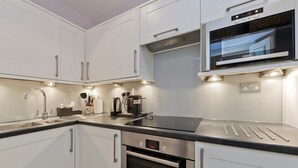 A modern kitchen with white cabinets, stainless steel appliances, and a built-in oven. - Spacious Studio Flat, Holland Park (Greater London)