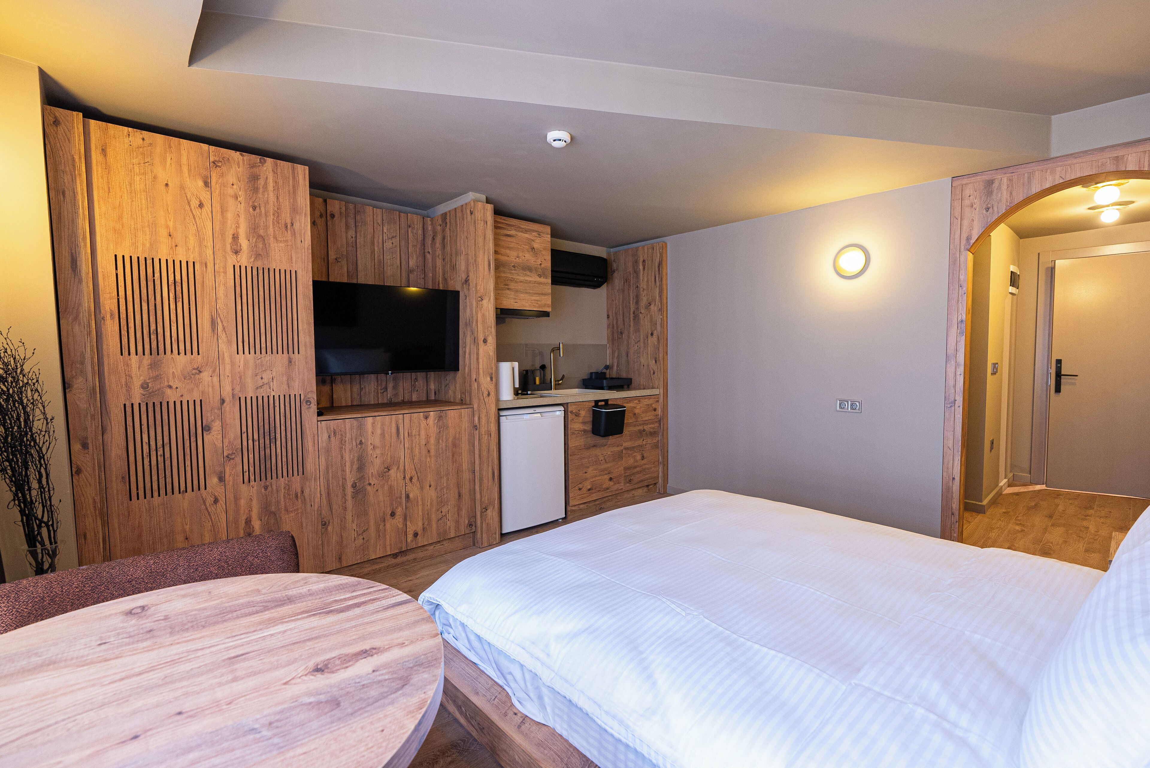 A compact hotel room with a bed, a small kitchenette, a TV, and a dining table.