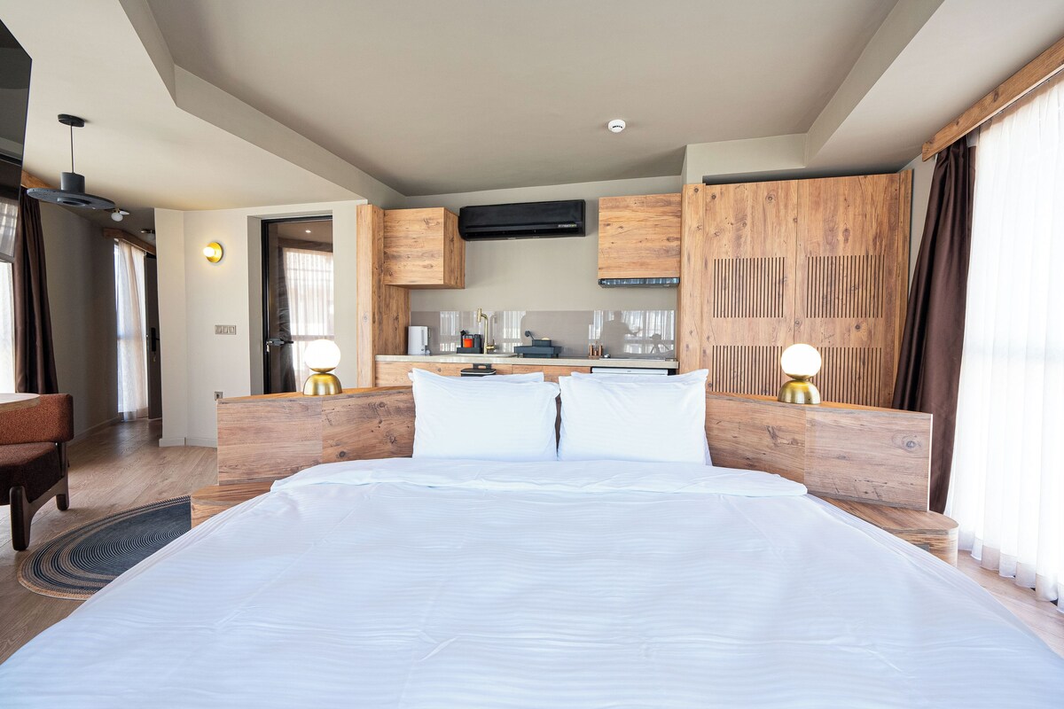 A hotel room with a large bed, wooden headboard, a desk, and a kitchenette.