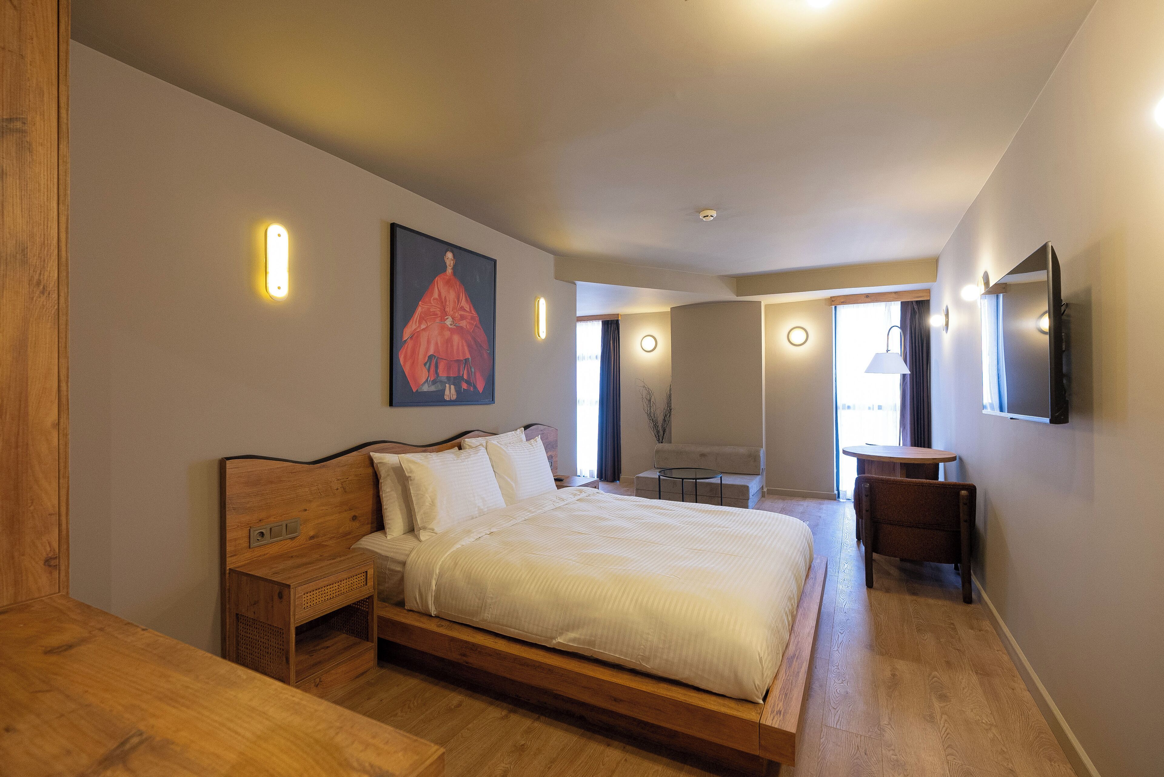 Un dormitorio moderno con una cama de madera, mesitas de noche, una mesa redonda y un televisor montado en la pared.