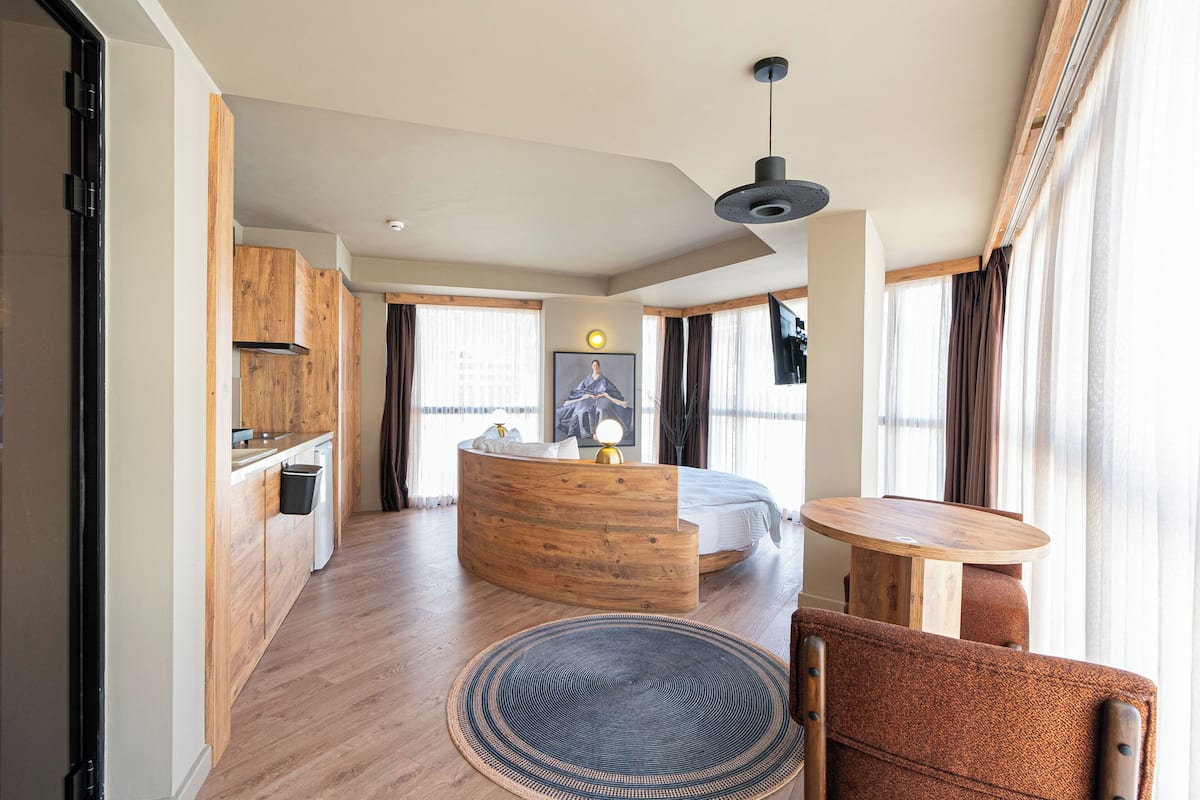 A modern interior with a kitchen, a round dining table, a sofa, and a bed.