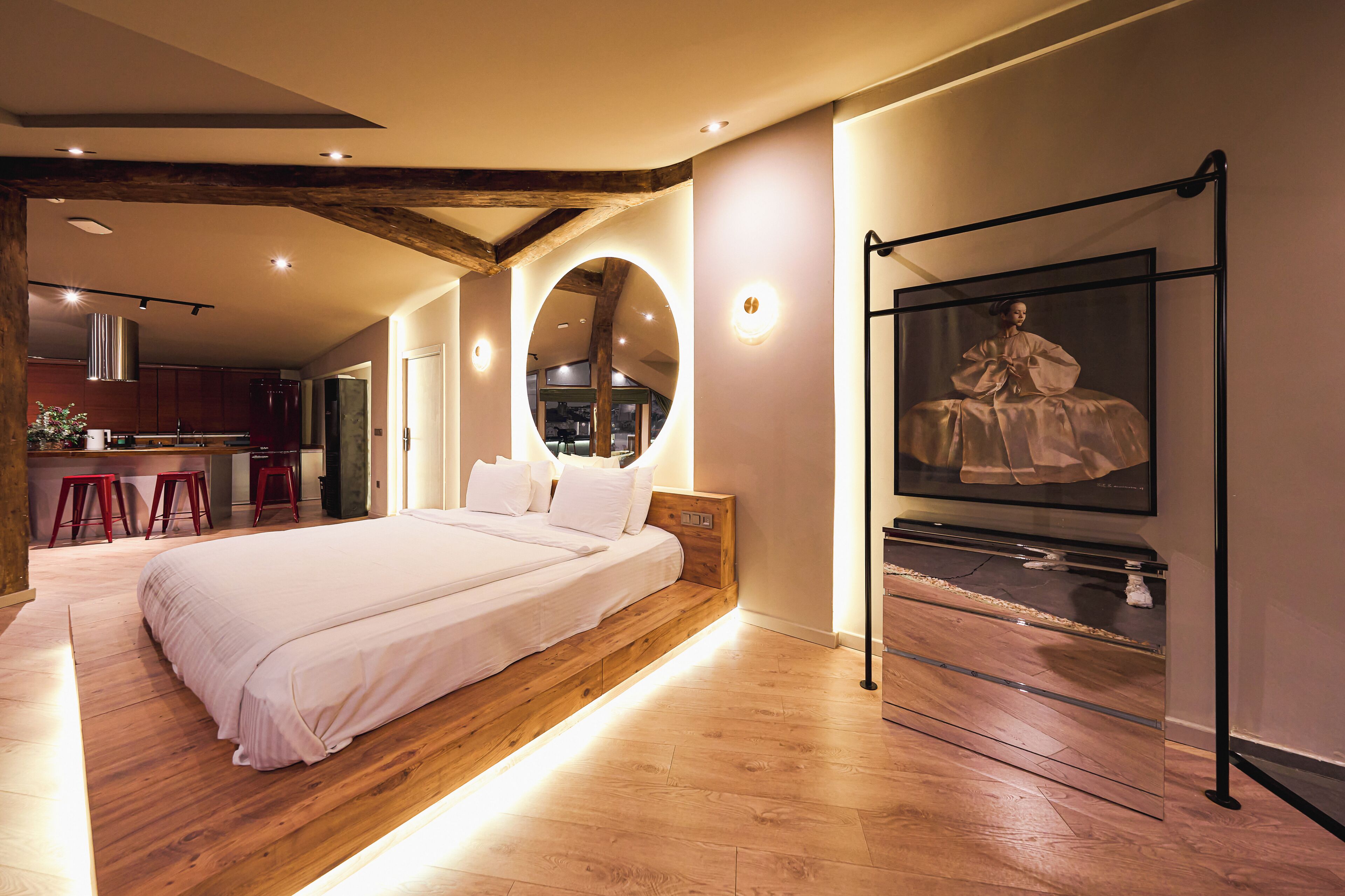 Un dormitorio moderno con una cama grande, vigas de madera, un espejo circular y una vitrina de vidrio.