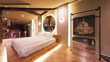 Un dormitorio moderno con una cama grande, vigas de madera, un espejo circular y una vitrina de vidrio.