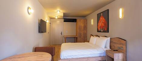 Quarto de hotel moderno com cama de madeira, uma pequena mesa de madeira, televisão fixada na parede e um quadro.