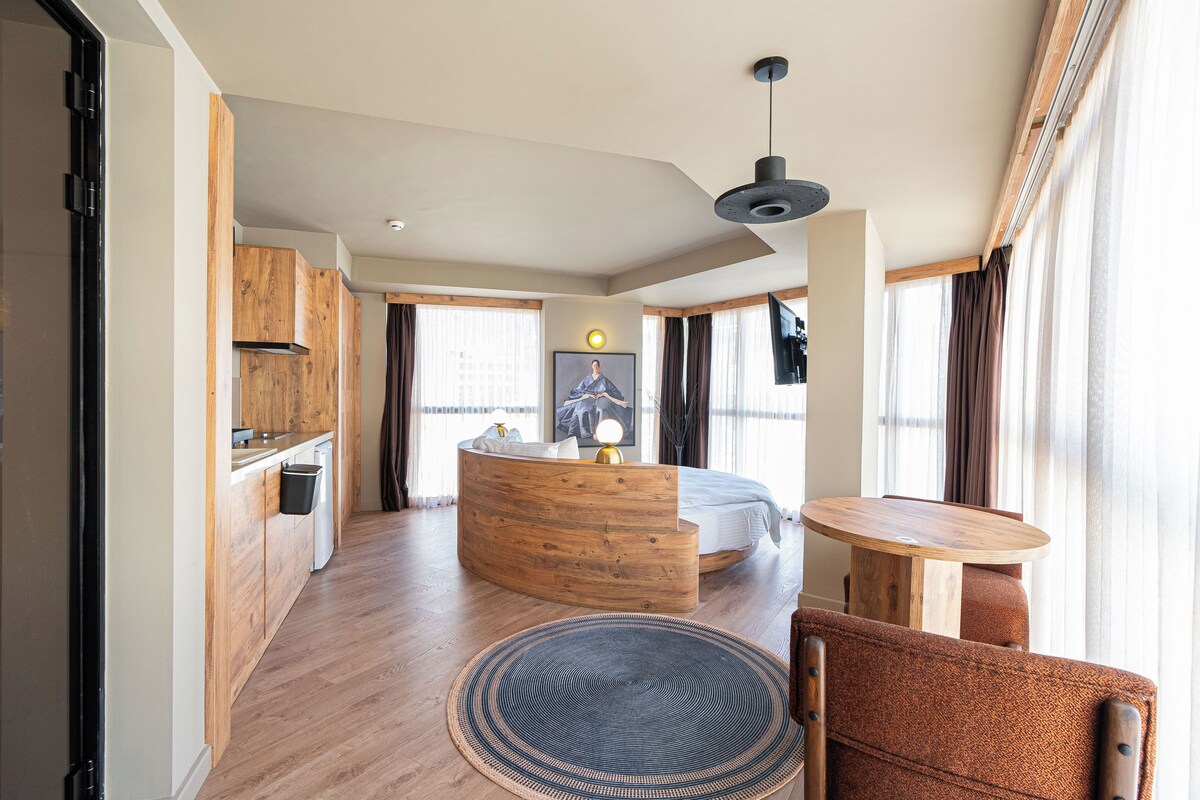 A modern interior with a kitchen, a round dining table, a sofa, and a bed.