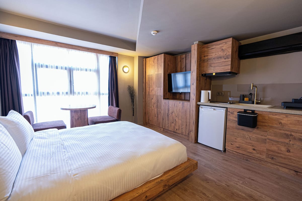 A hotel room with a bed, a small kitchenette, a TV, and a window with curtains.