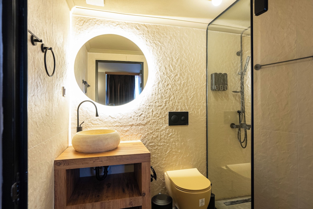 A bathroom with a round mirror, wooden vanity, and a toilet.