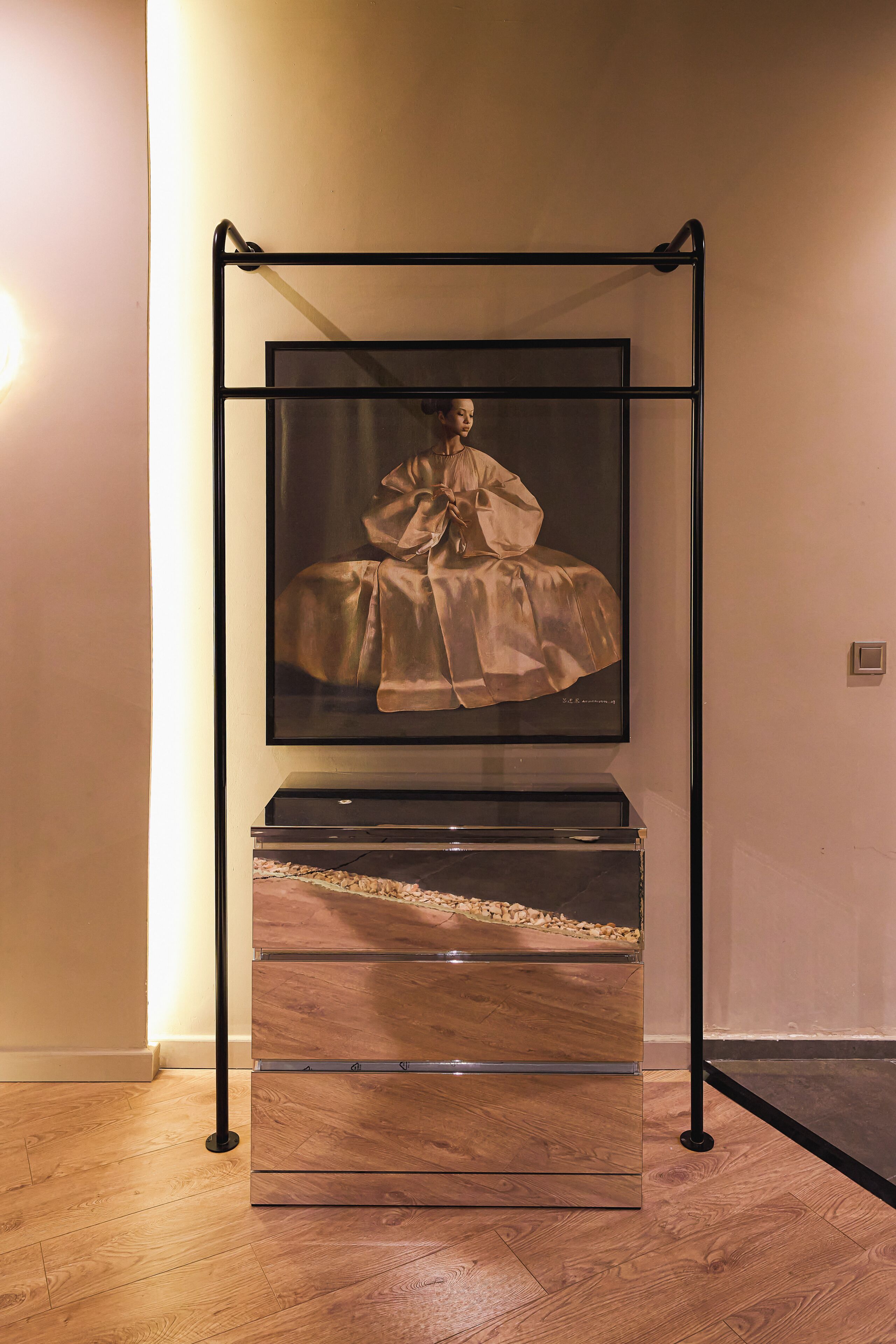 A framed artwork of a woman in a dress on a stand with a mirrored cabinet below.