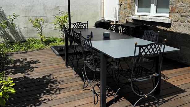 Un patio al aire libre con una mesa, sillas, un paraguas grande y un muro de piedra.