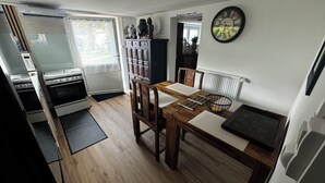 Una cocina compacta con una mesa de comedor, sillas de madera, un reloj negro y un radiador.