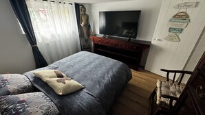 Un dormitorio con una cama, televisión, cómoda de madera y una silla.