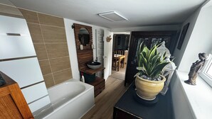 Un baño moderno con bañera, tocador de madera y una planta en maceta.