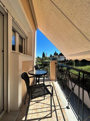 A balcony with a table and chairs, a view of a distant building, and a clear sky.