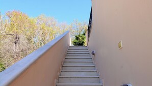 A staircase leading upwards, flanked by beige walls, with a clear blue sky above and dry vegetation in the background. - Elli Cozy House (Corfu)