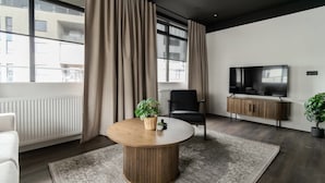 A modern living room with a round wooden table, a black chair, a television, and a potted plant.