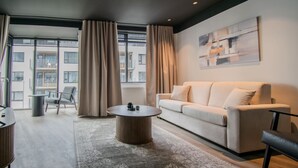 A modern living room with a sofa, coffee table, and a view of a building through large windows.
