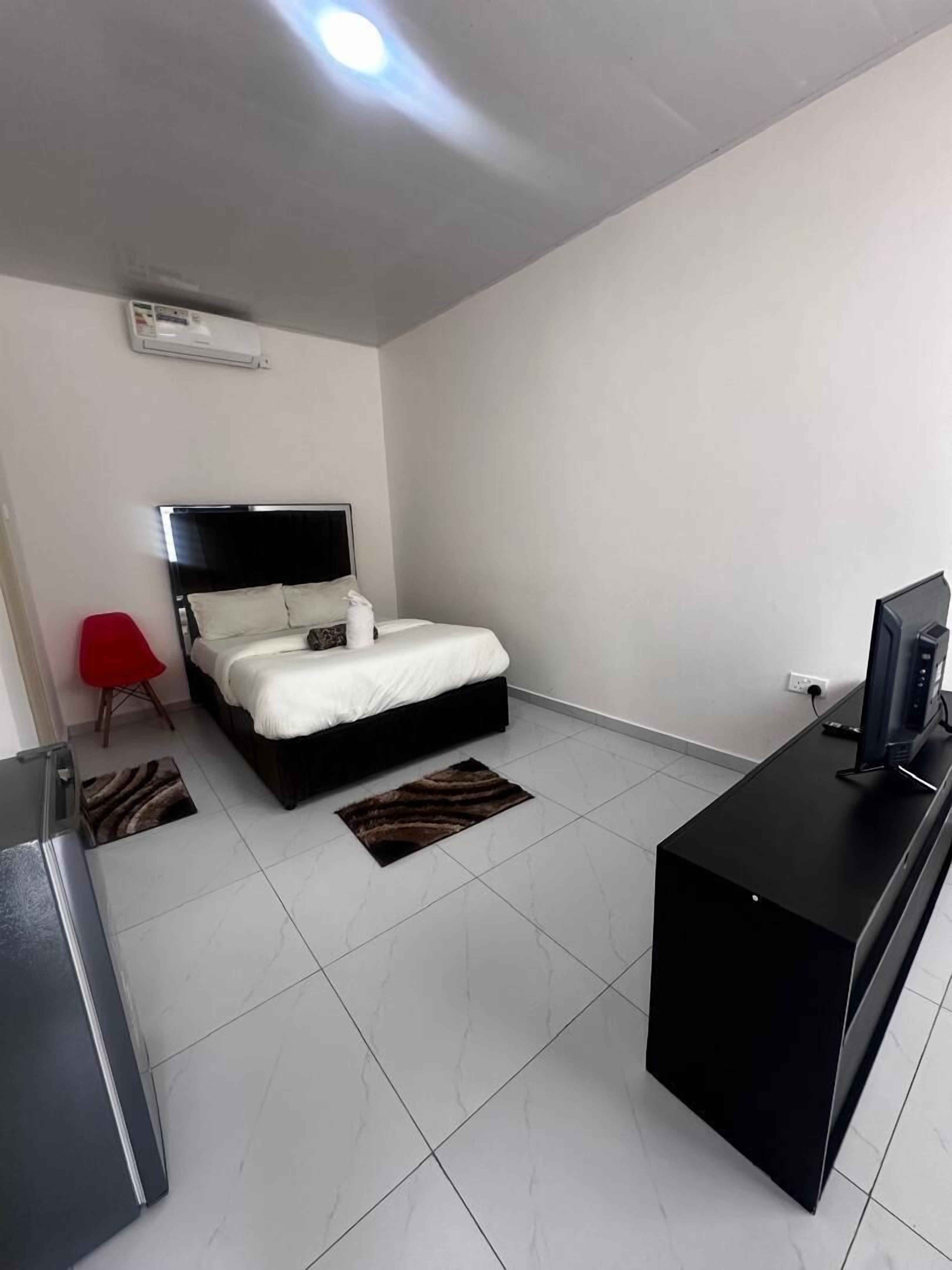 Una habitación de hotel moderna con una cama, un escritorio con computadora, una silla roja y un televisor.
