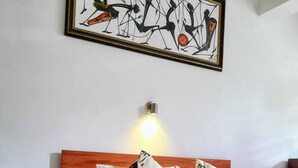 Une chambre avec un lit en bois, une literie blanche et une couverture aux couleurs vives. Un luminaire est fixé au mur au-dessus du lit.
