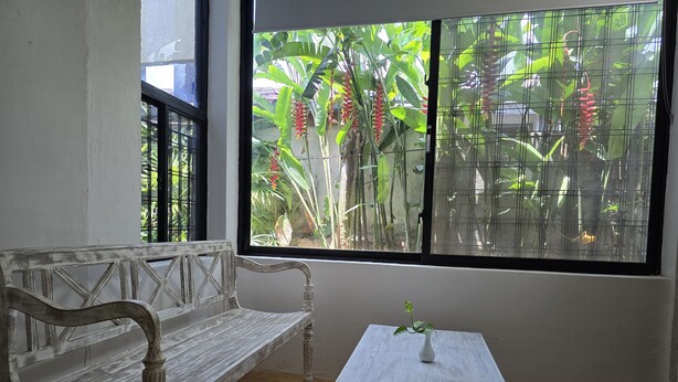 Une pièce avec un banc blanc, une petite table sur laquelle est posée une plante, et une fenêtre donnant sur un paysage verdoyant.