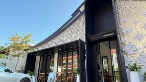 Un edificio moderno con fachada de vidrio, zona de estar al aire libre y un letrero que indica un restaurante.