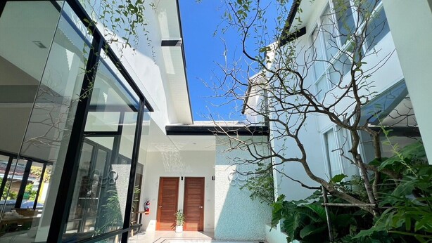 Un edificio moderno con piscina de cristal, puertas de madera y abundante vegetación.