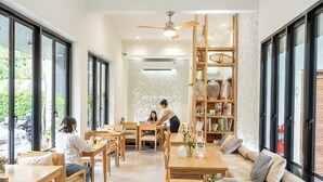 Un café moderno con muebles de madera, ventanas amplias y una estantería decorativa con frascos.