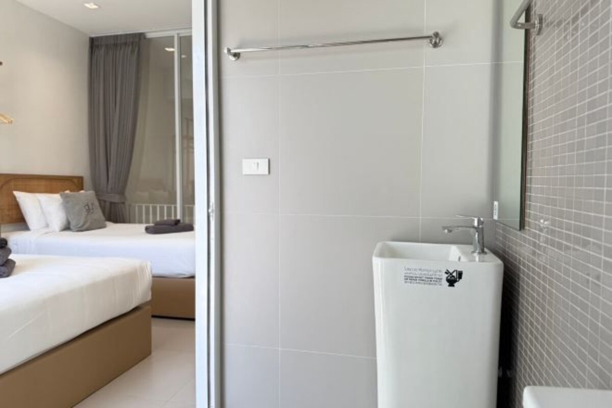 A hotel room with a bed, a bedside table, a large window with curtains, and a bathroom with a sink and mirror.