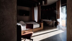 A modern hotel room with a large bed, a sitting area, a bathtub, and a view of the outdoors.