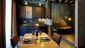 A modern kitchen with dark cabinets, a dining table set for two, and a cozy seating area with a sofa and a lamp.