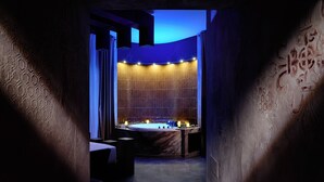 A modern spa room with a large bathtub, a seating area, and a wall with intricate patterns.