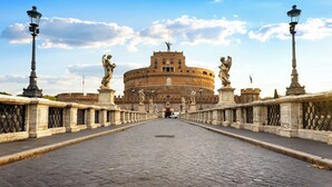 A cobblestone bridge leading to a historic building with statues on either side.